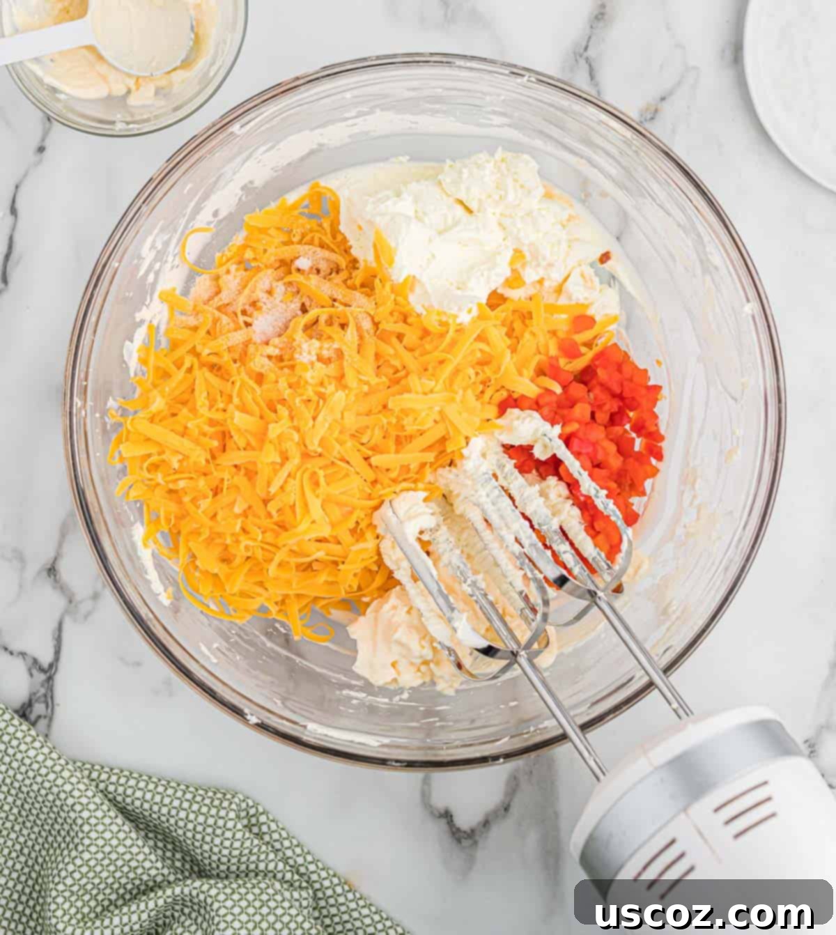 Pimento Cheese 6 Various ingredients for pimento cheese, including freshly grated cheddar, drained pimentos, and spices, being added to the whipped cream cheese in a mixing bowl.