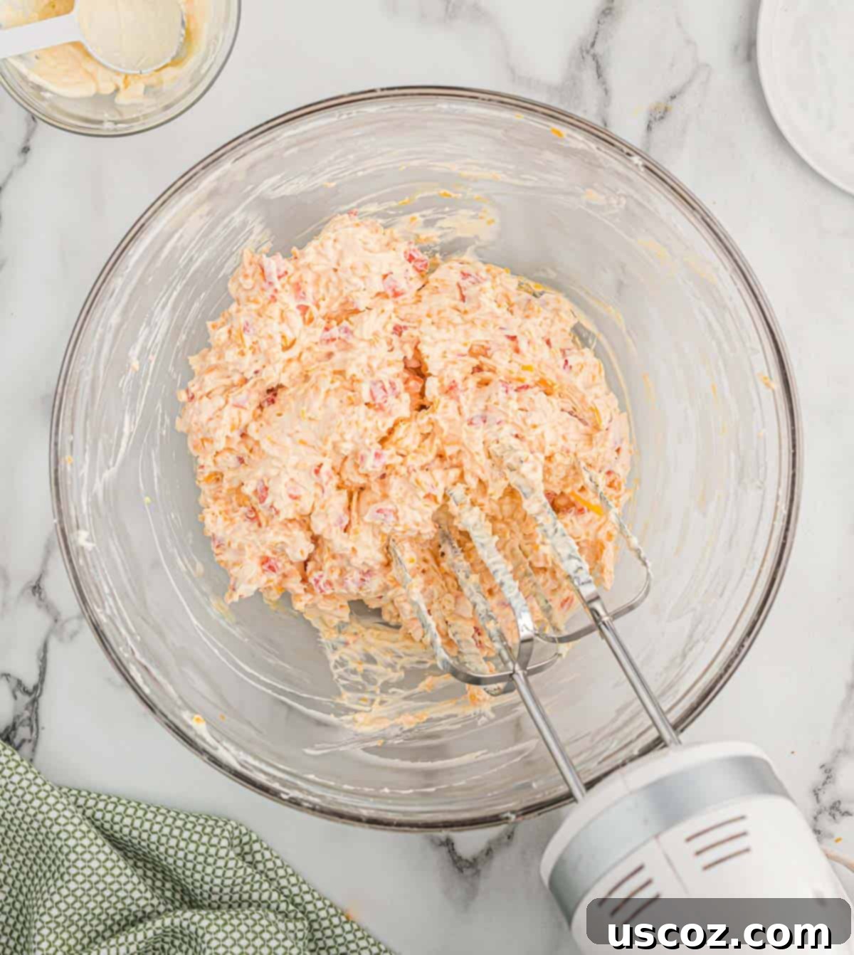 Pimento Cheese 7 Close-up of pimento cheese being mixed in a clear glass bowl, showcasing the creamy texture and vibrant red pimento pieces.