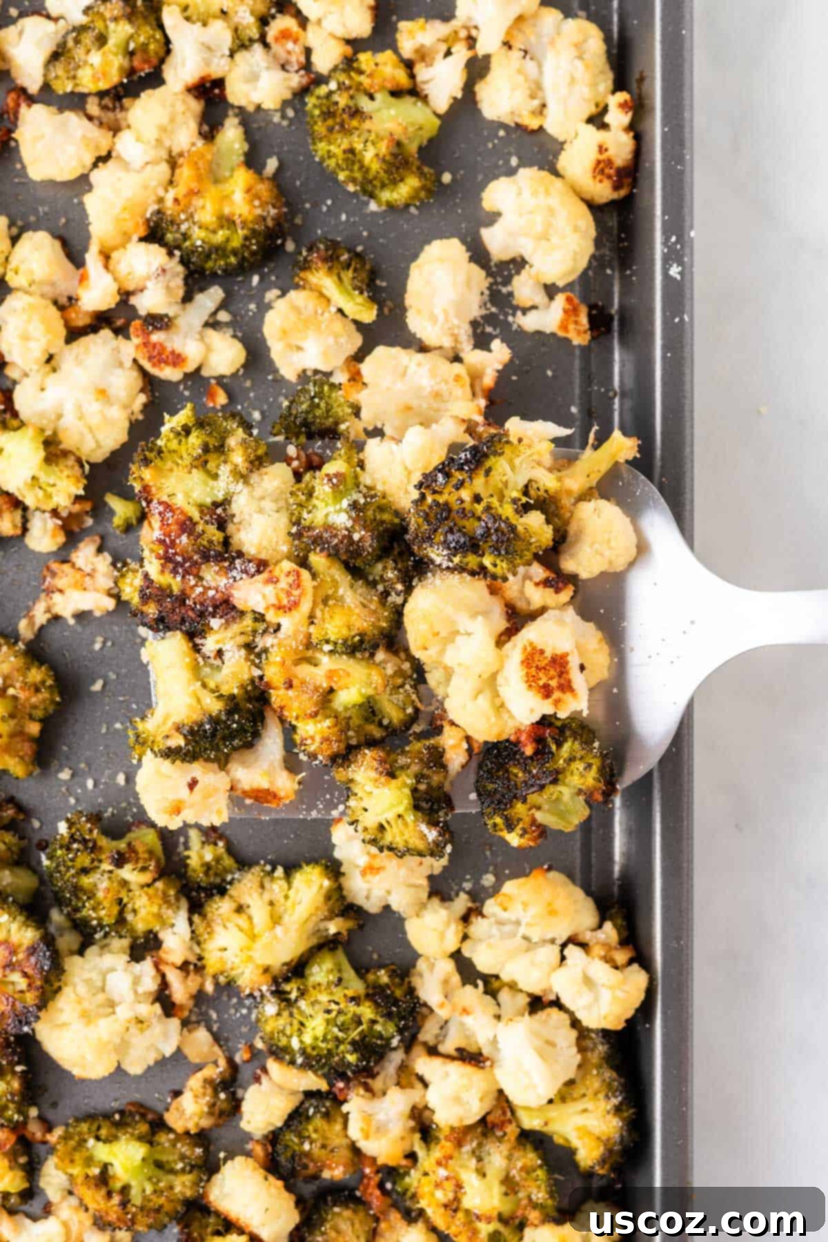 Golden Roasted Broccoli and Cauliflower 2 Spatula carefully lifting golden-brown, crispy roasted broccoli and cauliflower florets from a baking pan, ready to be served.