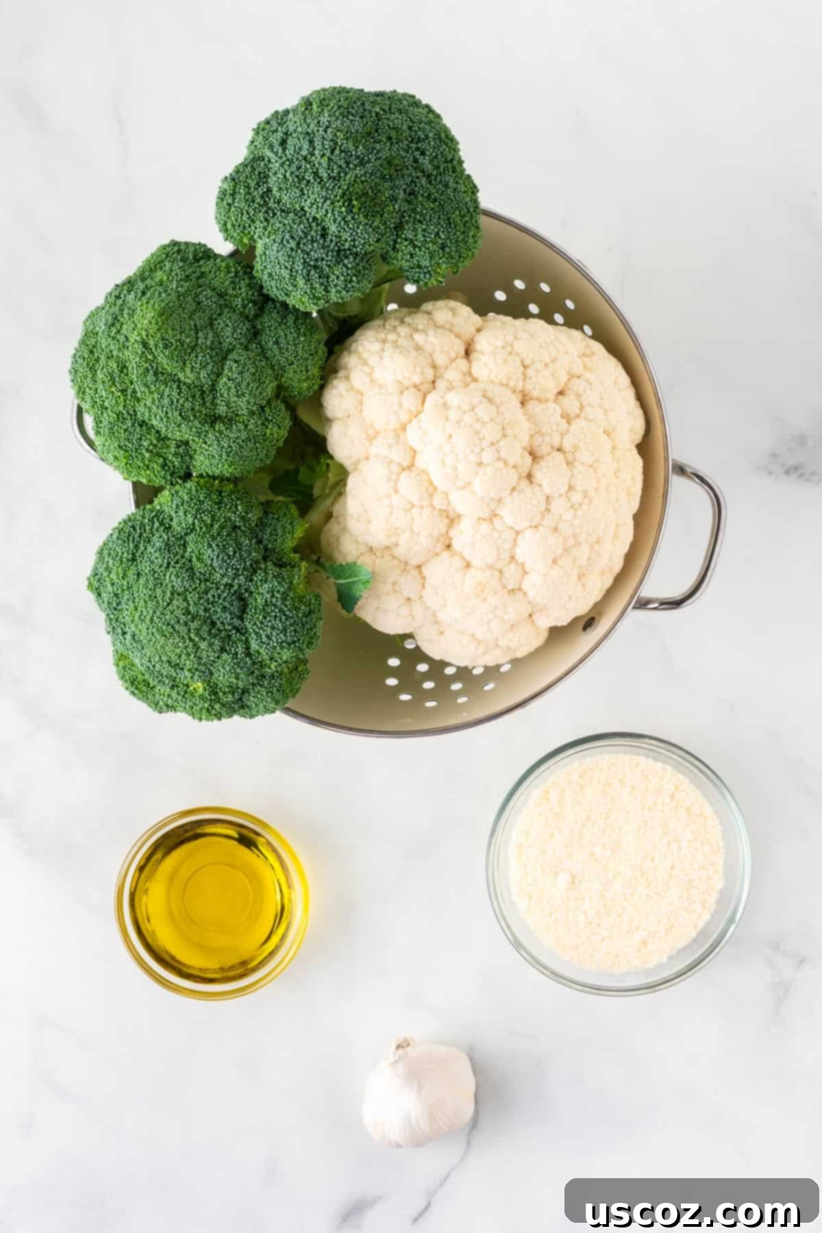Golden Roasted Broccoli and Cauliflower 3 A flat lay of all the essential ingredients: fresh broccoli florets, cauliflower florets, a pile of minced garlic, a bowl of powdered parmesan cheese, and a bottle of olive oil, arranged neatly on a wooden surface.