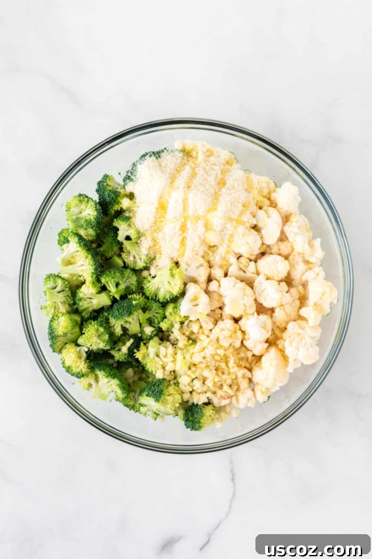 Golden Roasted Broccoli and Cauliflower 6 Minced garlic, powdered parmesan cheese, and olive oil being drizzled and sprinkled over broccoli and cauliflower florets in a mixing bowl.