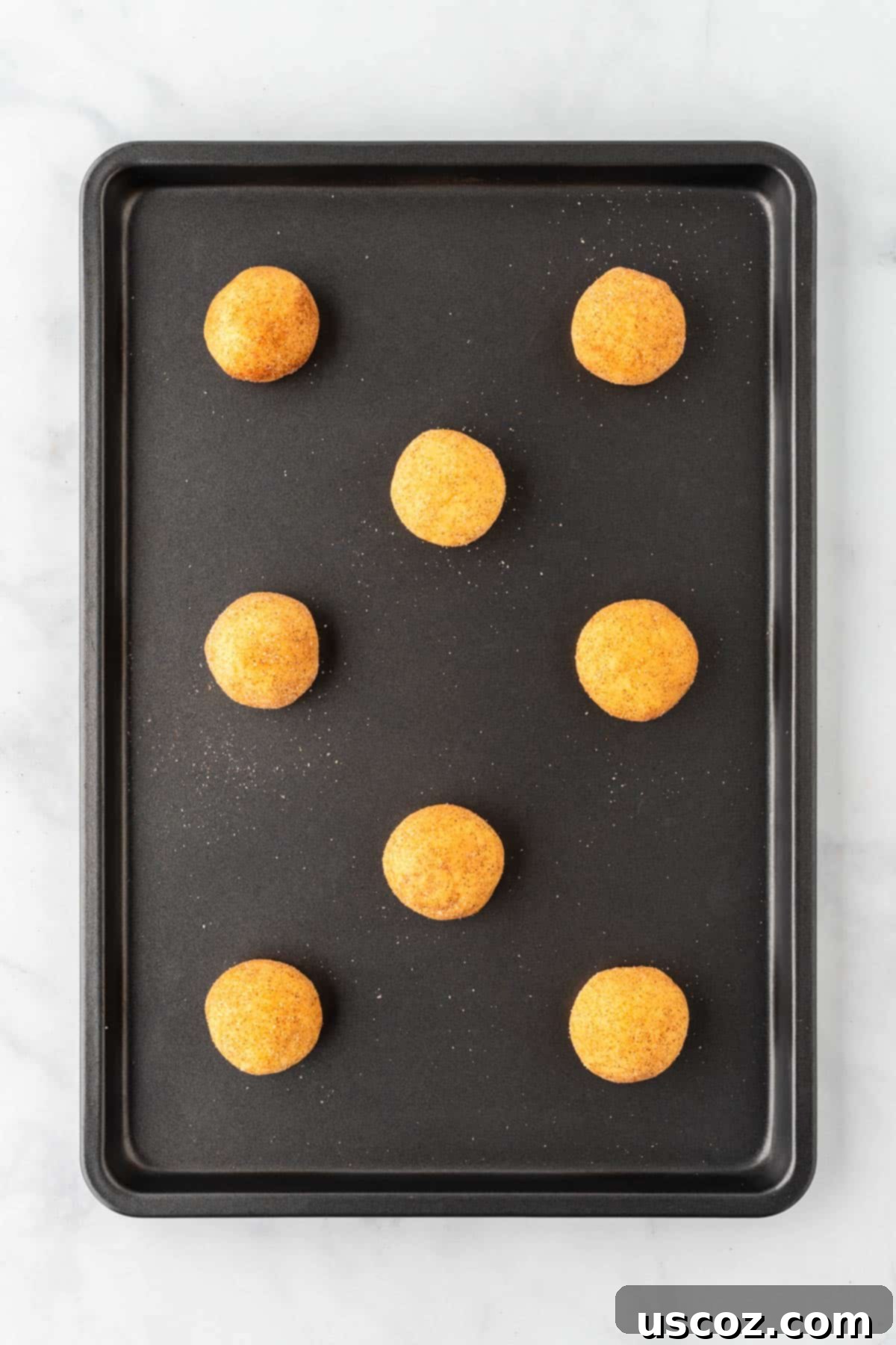 Effortless Cake Mix Snickerdoodles 11 Unbaked cookie dough balls coated in cinnamon sugar, arranged on a baking sheet