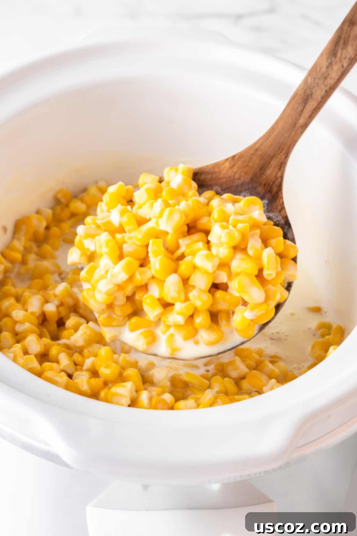 Velvety Slow Cooker Creamed Corn 11 wooden spoon taking creamed corn from the slow cooker