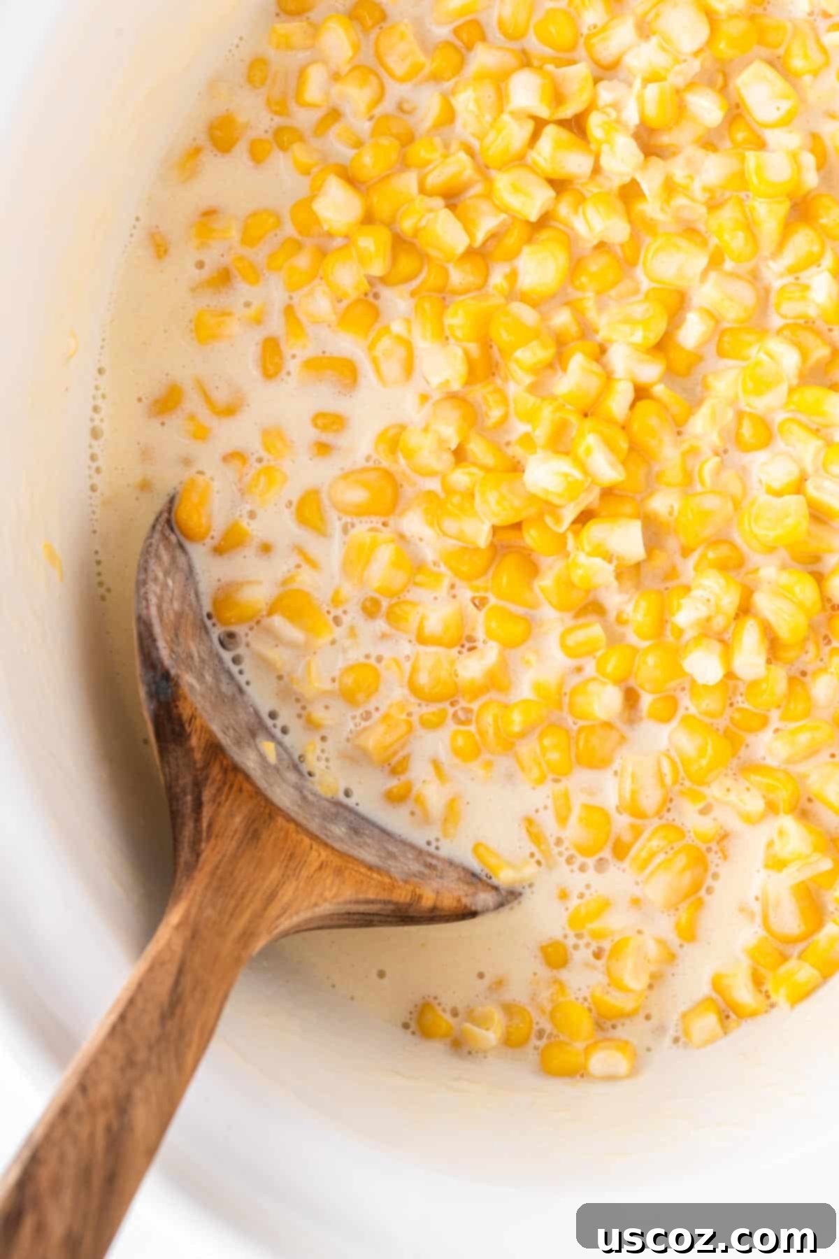 Velvety Slow Cooker Creamed Corn 3 wooden spoon taking creamed corn from the slow cooker