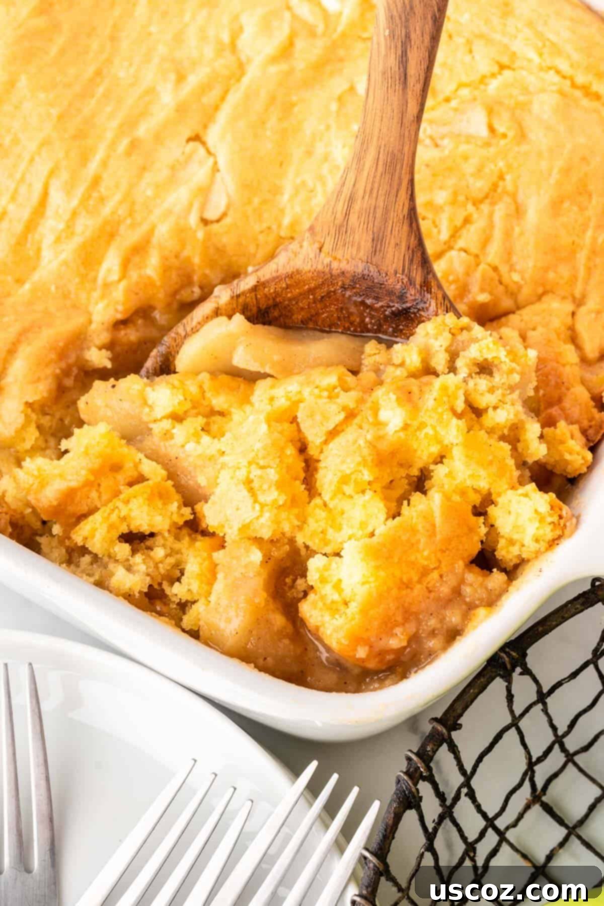 Effortless Apple Cobbler 13 A wooden spoon scooping out a generous portion of warm apple cobbler from the baking dish, showing the tender apple filling and the cake topping.