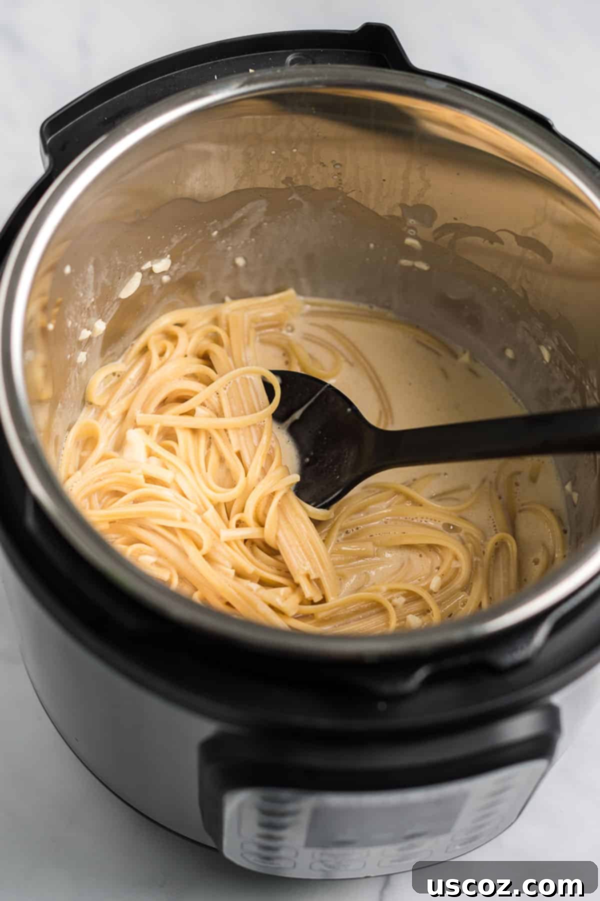 Quick and Creamy Instant Pot Pasta 7 Close-up of stirring the cooked linguine noodles into the newly added cream and cheese to form a rich sauce.
