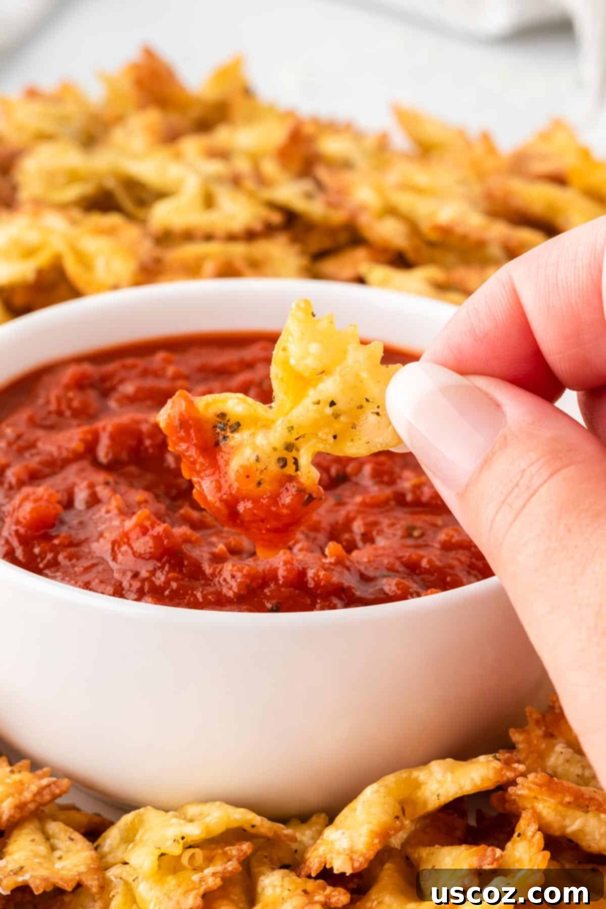 Crispy Air Fryer Pasta Chips 13 A hand dipping a crispy air fryer pasta chip into a bowl of marinara sauce.