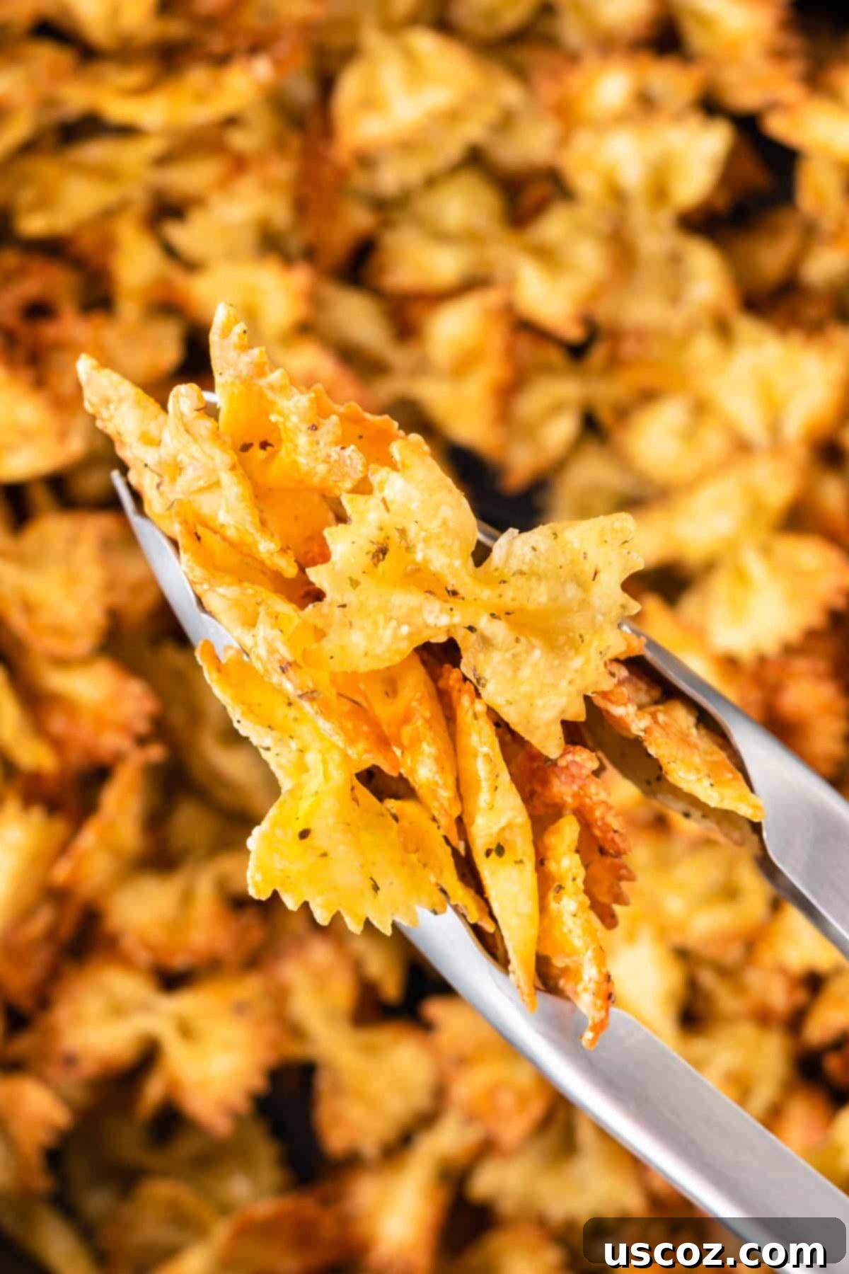 Crispy Air Fryer Pasta Chips 14 Tongs carefully removing a batch of perfectly air fried pasta chips from the air fryer basket, showcasing their golden crispness.