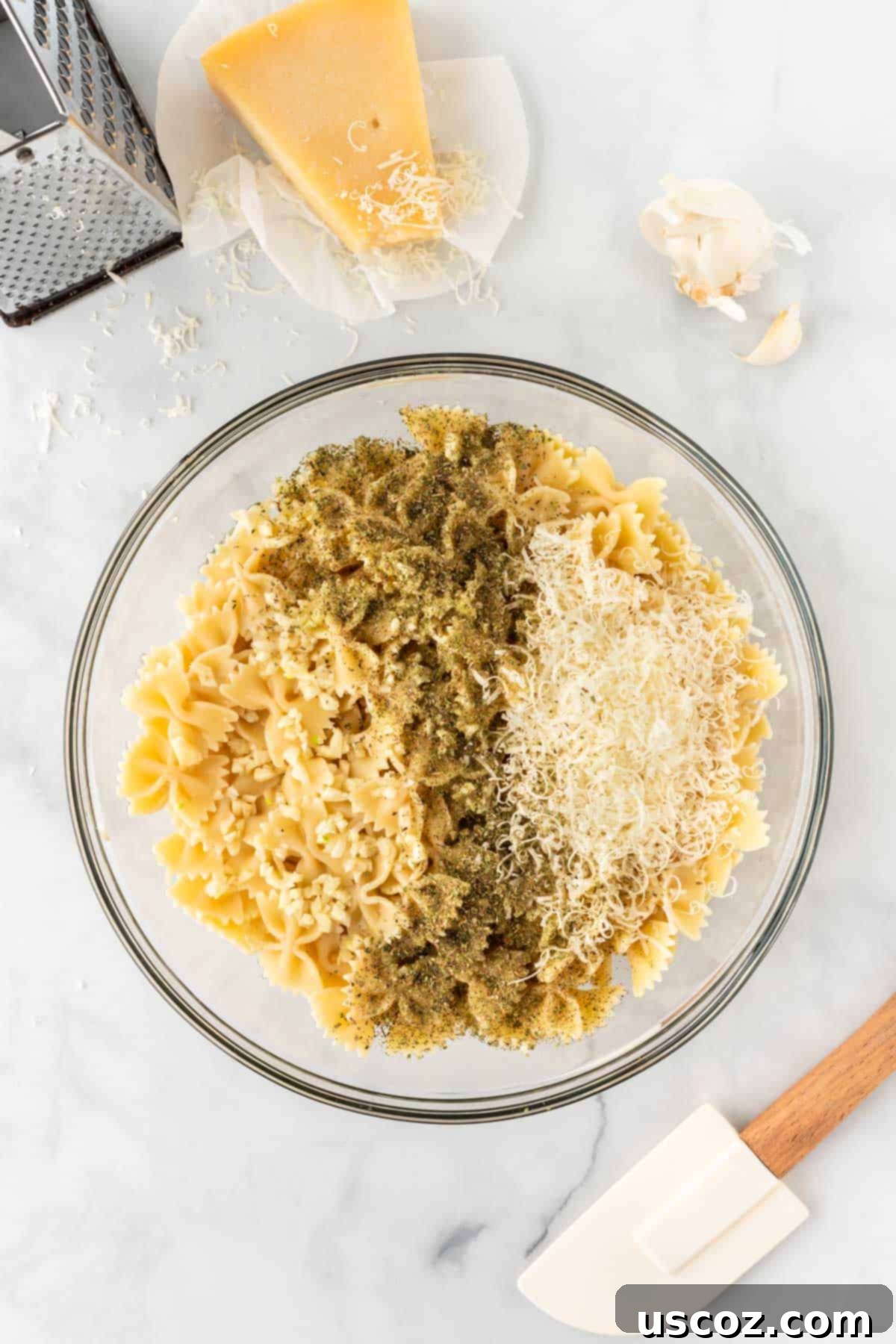 Crispy Air Fryer Pasta Chips 7 Adding minced garlic, Italian seasoning, and parmesan cheese to cooked bowtie pasta in a mixing bowl.