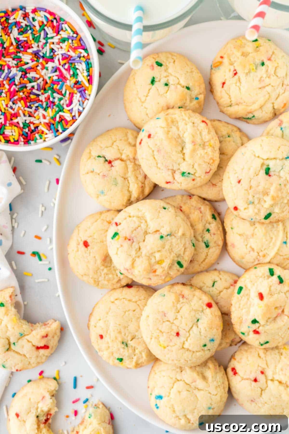 Effortless Rainbow Cake Cookies 3 A white platter filled with perfectly baked, golden-brown funfetti cookies adorned with colorful sprinkles.