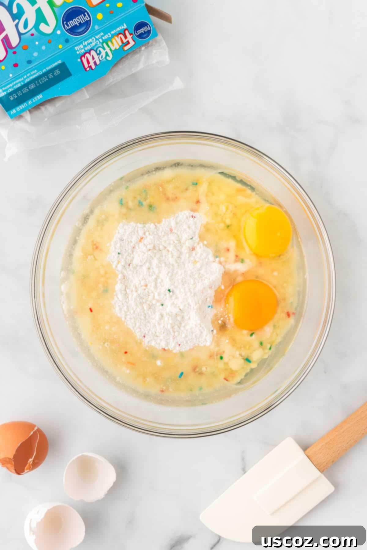 Effortless Rainbow Cake Cookies 6 The process of adding eggs and oil to the funfetti cake mix in a mixing bowl, demonstrating the simple ingredient combination.