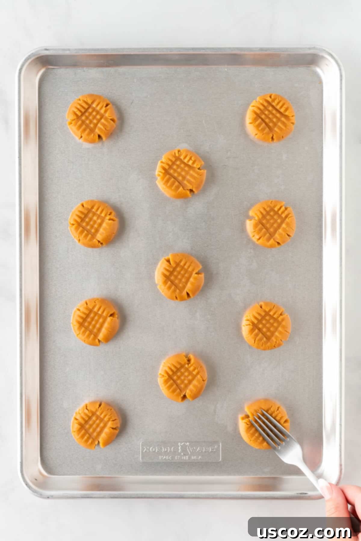 Easy Cake Mix Peanut Butter Cookies 11 A fork being used to press the classic criss-cross pattern onto a peanut butter cookie dough ball.