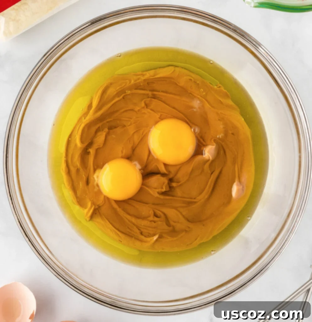 Easy Cake Mix Peanut Butter Cookies 5 Eggs, oil, and peanut butter are placed together in a mixing bowl, ready to be combined.