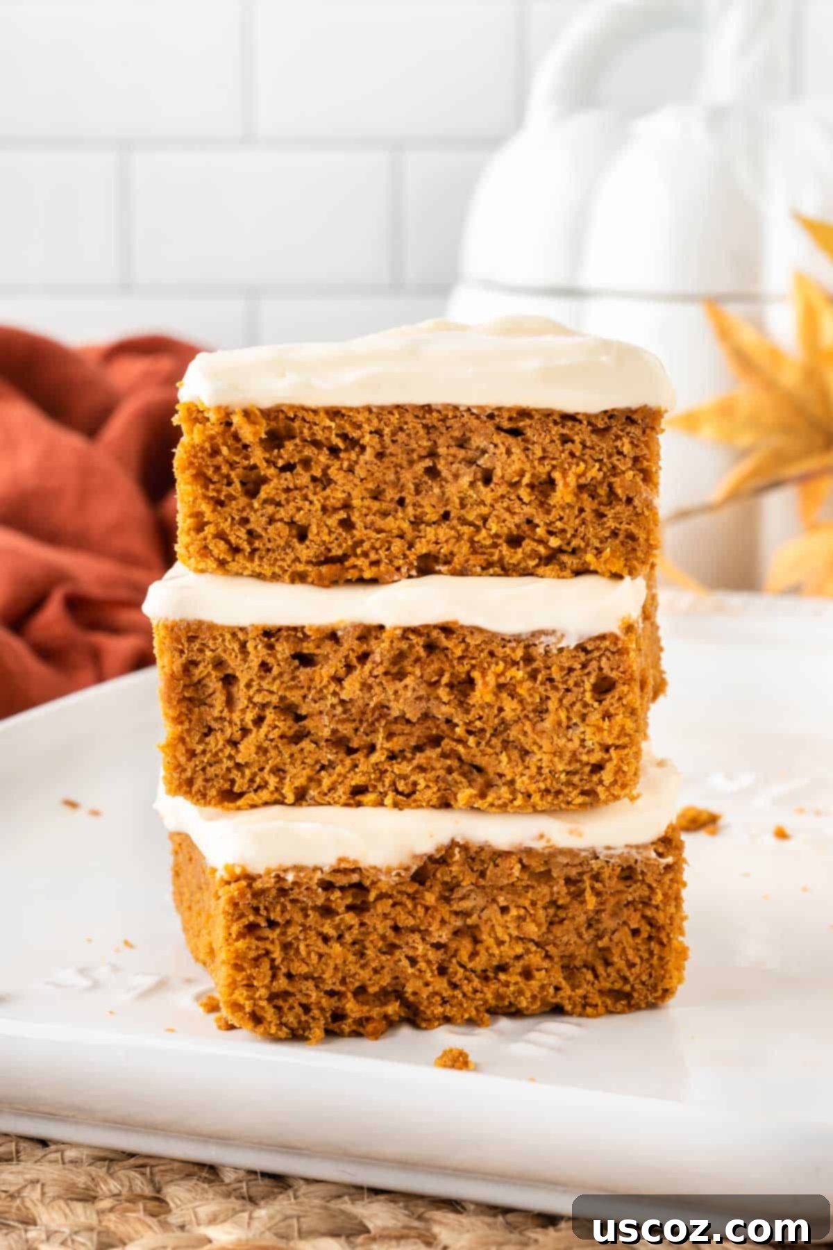 Easy Cake Mix Pumpkin Bars 12 three cake mix pumpkin bars stacked on a plate, showing the generous frosting