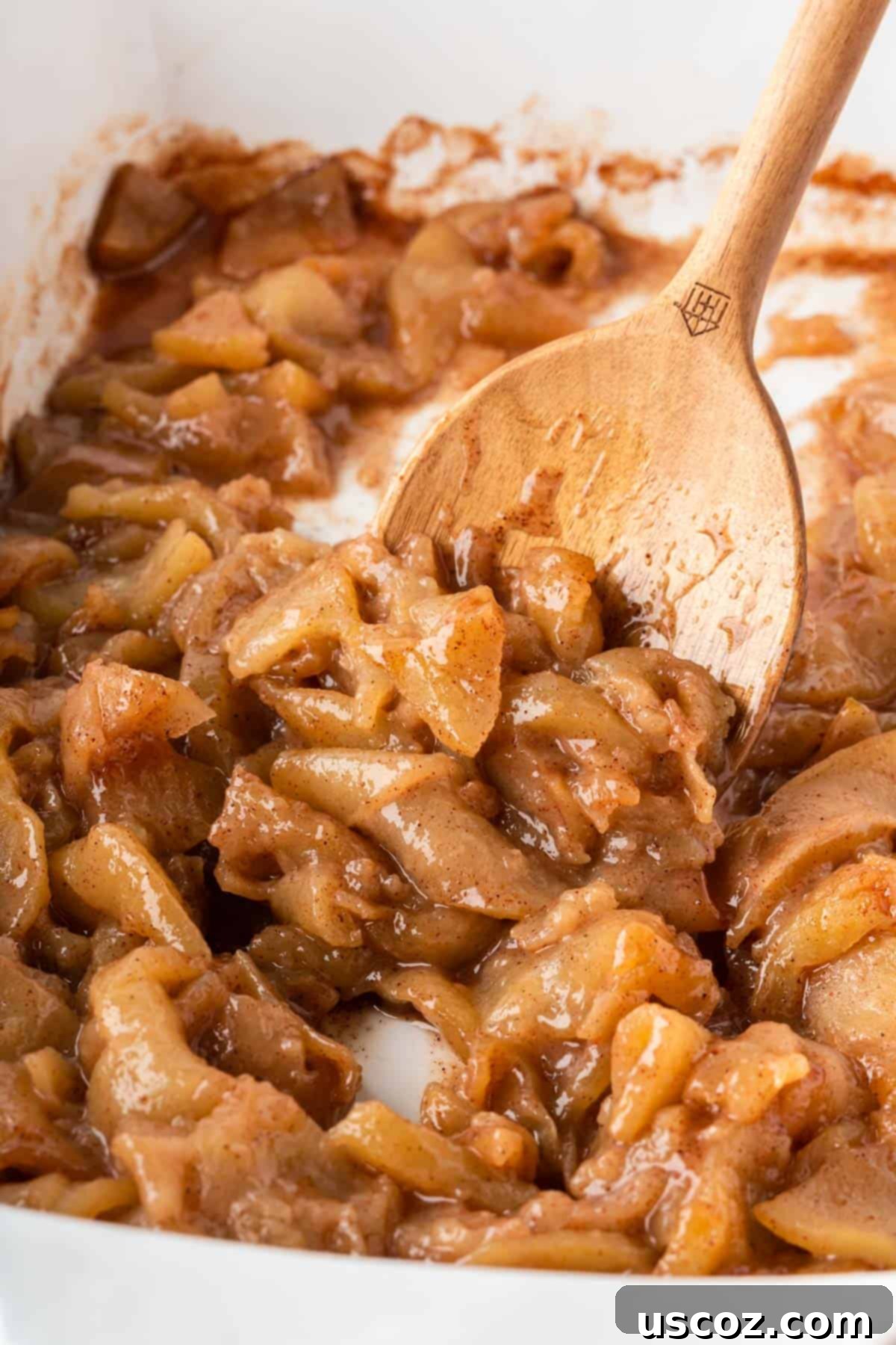 Warm Baked Cinnamon Apples 11 A wooden spoon scooping a portion of warm, glistening baked cinnamon apples from the baking dish.