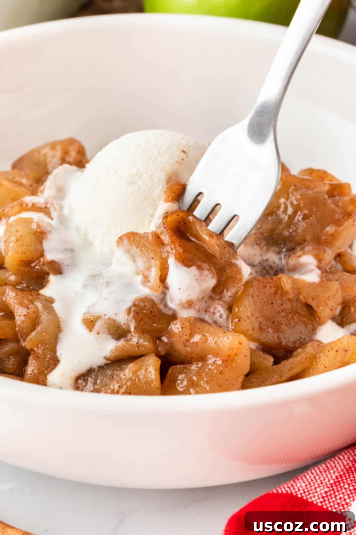Warm Baked Cinnamon Apples 12 A fork taking a bite of baked cinnamon apples with melted vanilla ice cream, showing the delicious caramel sauce.
