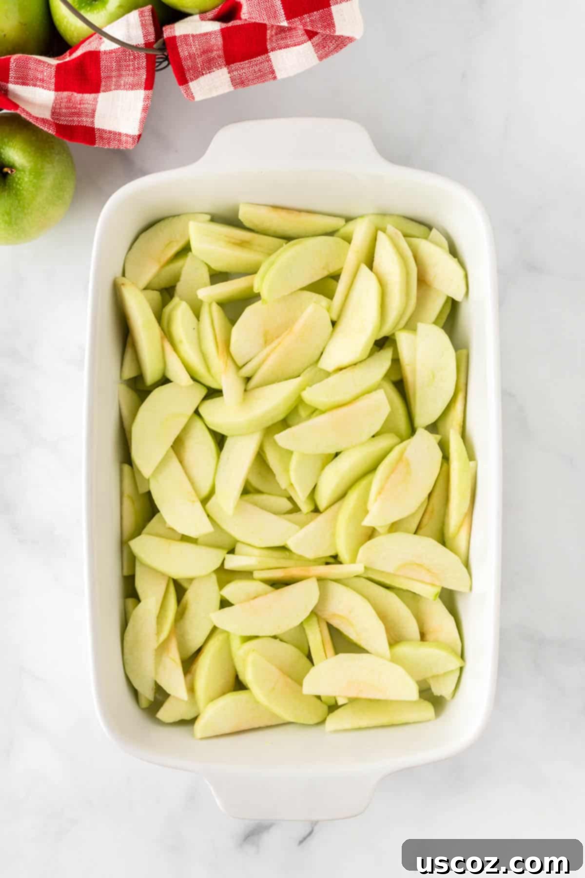 Warm Baked Cinnamon Apples 5 Thinly sliced apple pieces neatly arranged in a clear glass baking dish, ready for seasoning.