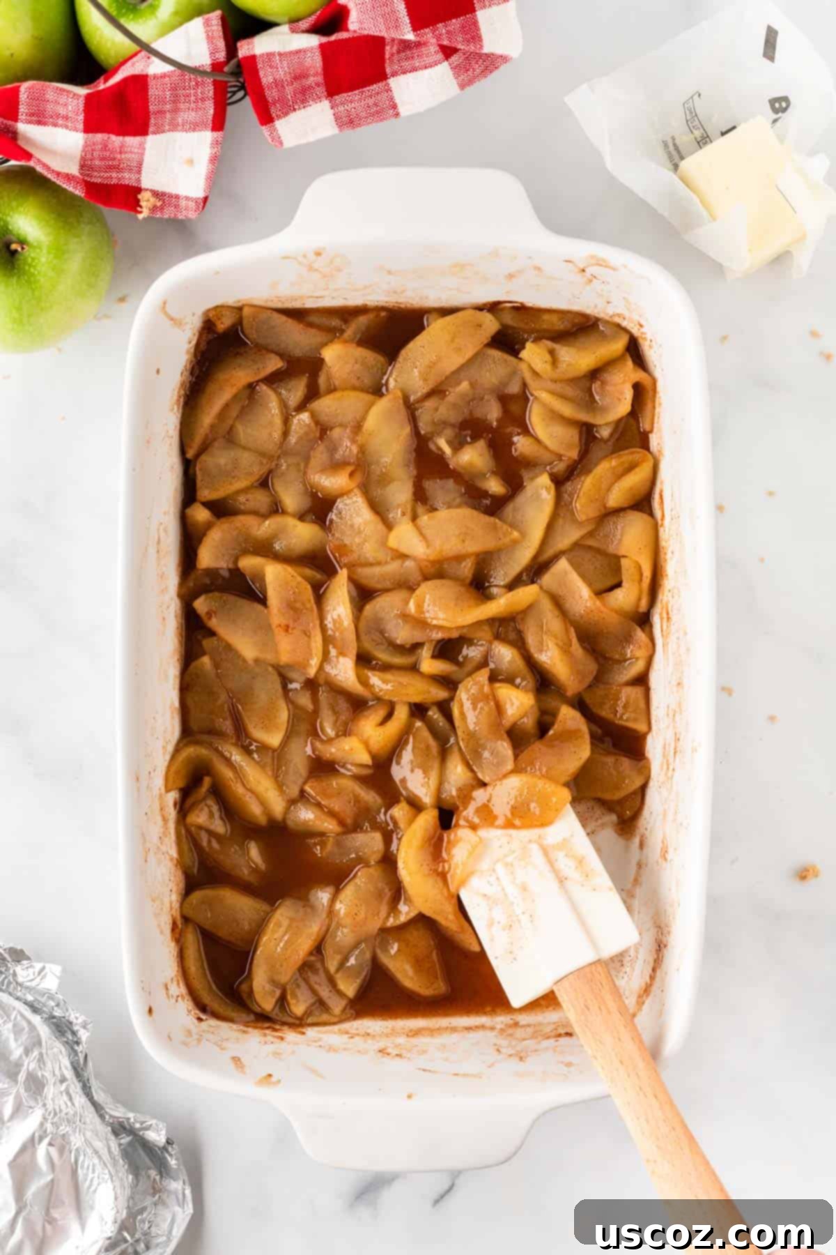 Warm Baked Cinnamon Apples 10 A wooden spoon stirring the baked cinnamon apples in the baking dish, showing the rich, bubbly caramel sauce.
