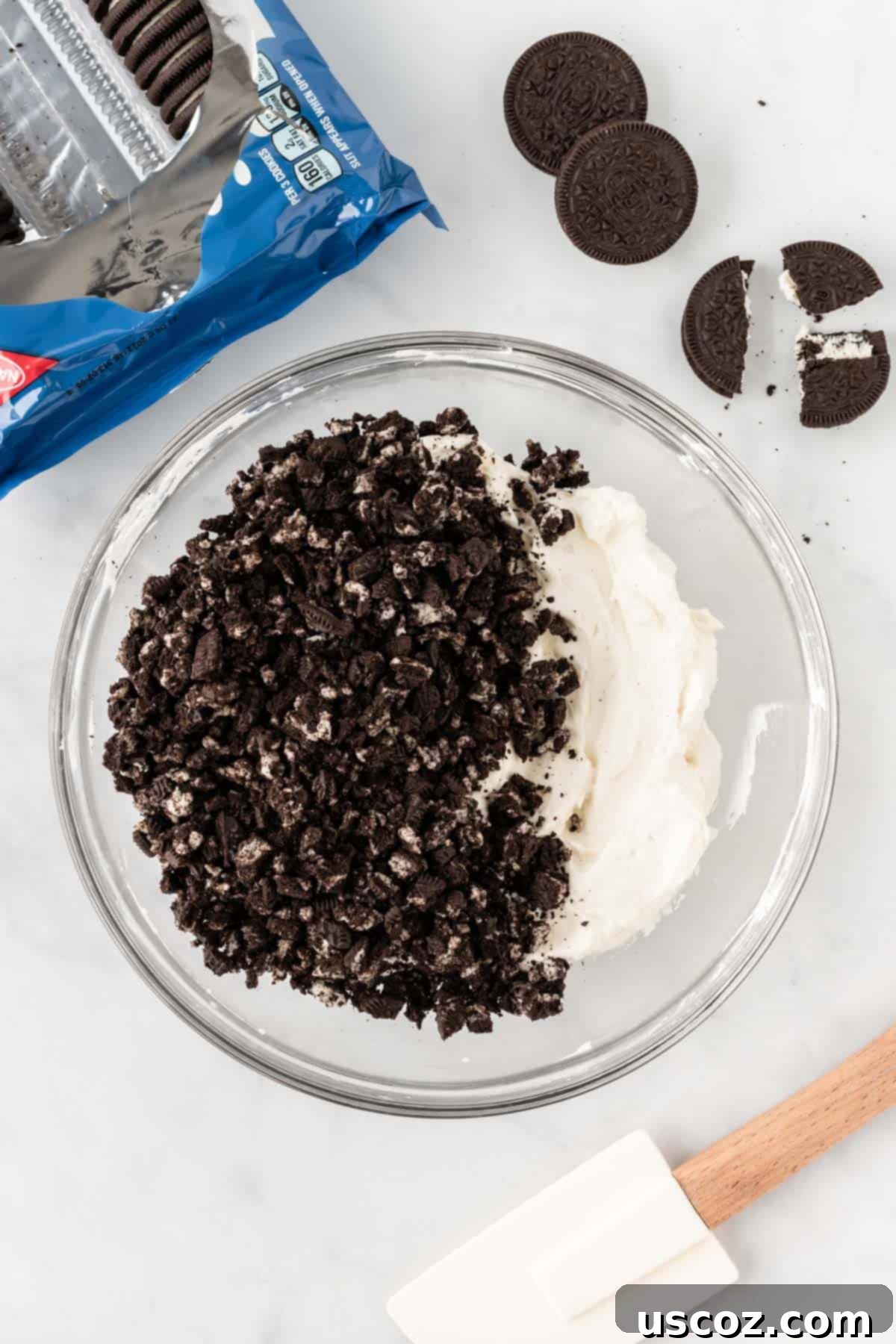 Oreo Bliss Pie 6 Crushed Oreo cookies being gently folded into the creamy whipped cream and cream cheese filling in a glass bowl.