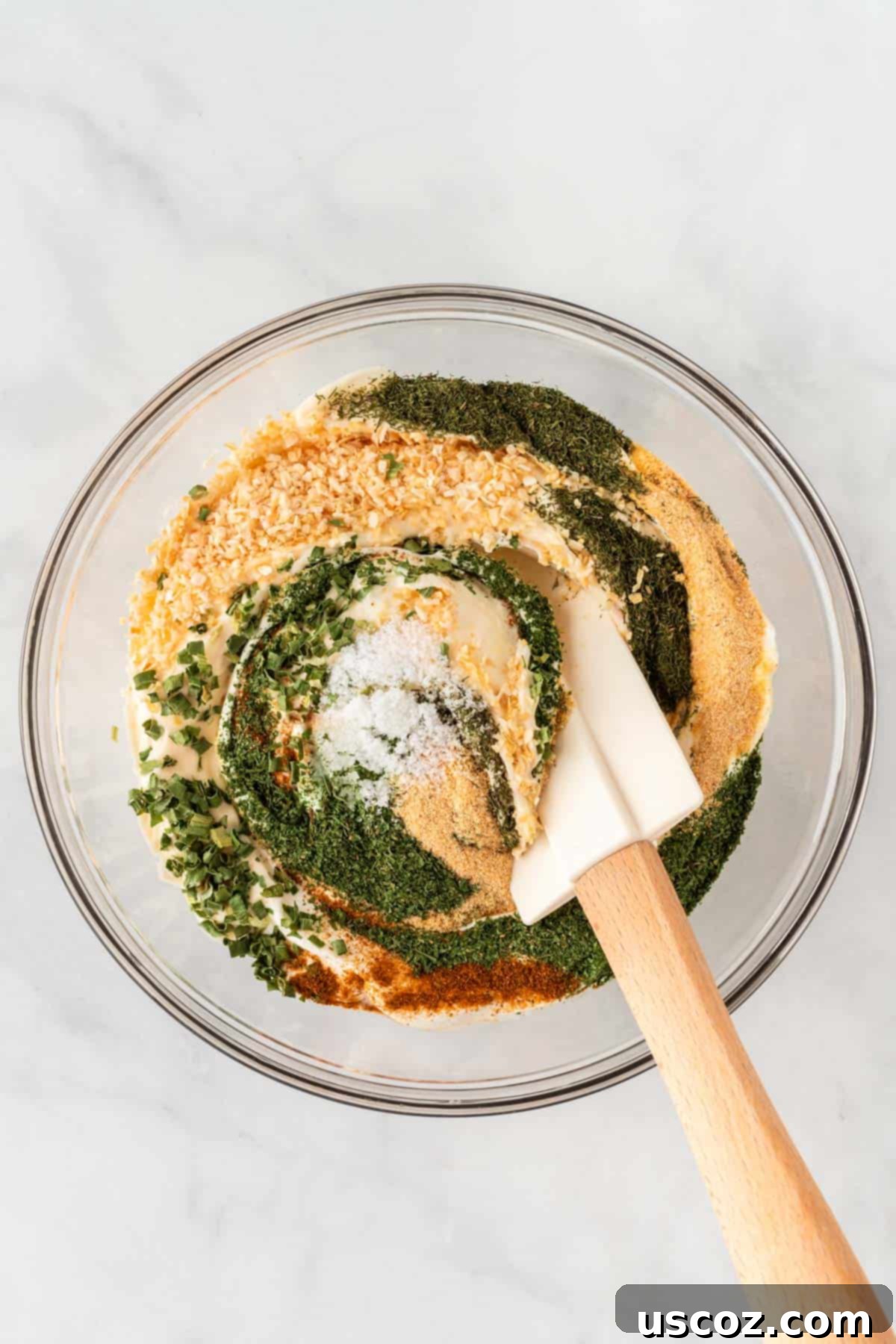Garden Fresh Dip 6 A hand stirring the creamy sour cream and mayonnaise base with a spatula, mixing in the various dried spices until well combined and smooth, creating the rich veggie dip.