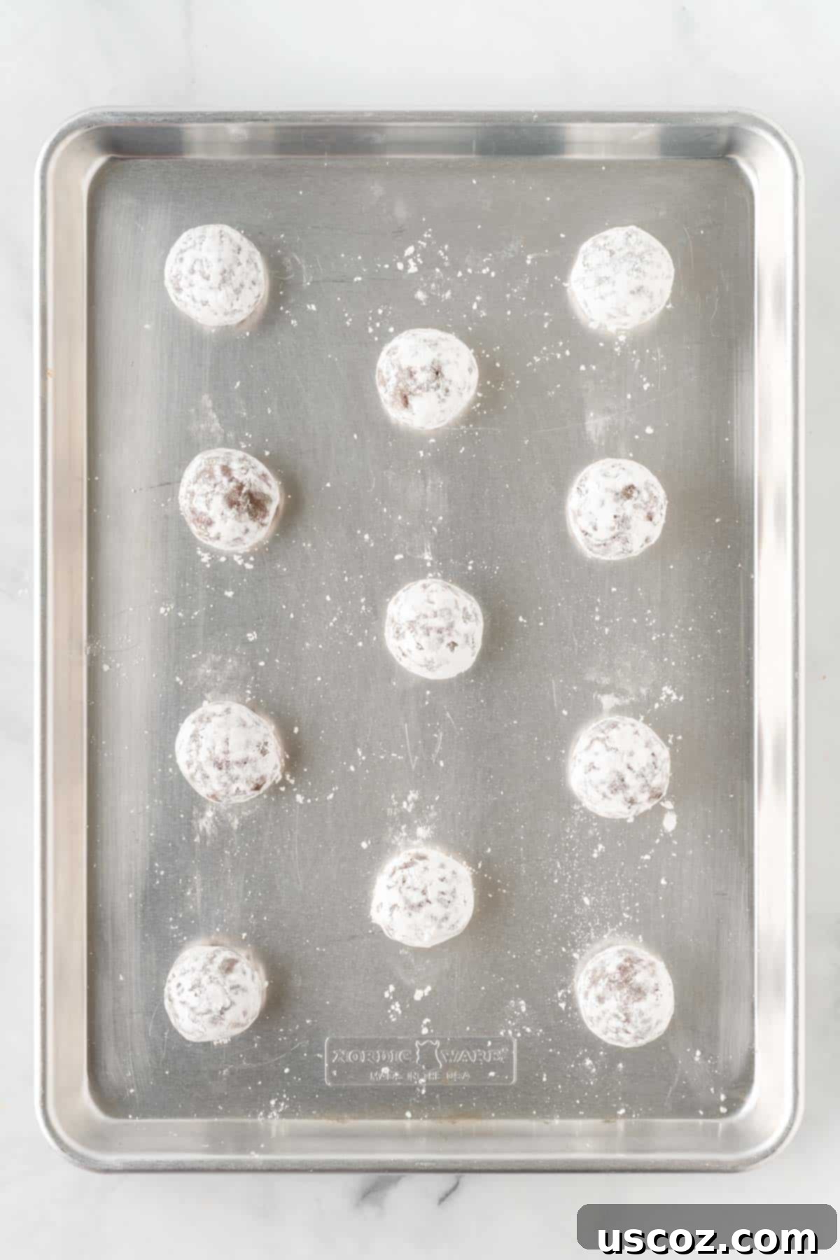 Irresistible Cake Mix Crinkles 10 cookie dough rolled in powdered sugar on a baking sheet