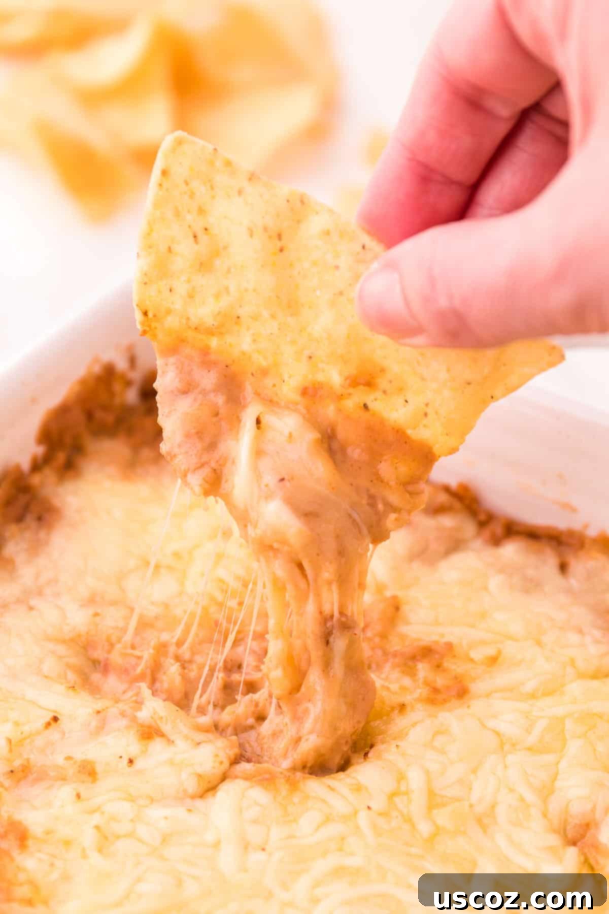 Rich Cream Cheese Bean Dip 2 Dipping a tortilla chip into a warm, bubbly cream cheese bean dip topped with melted cheese