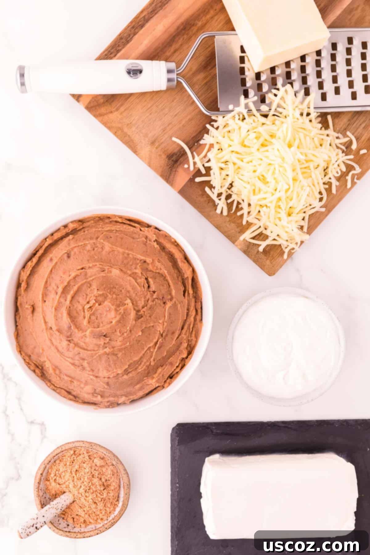 Rich Cream Cheese Bean Dip 3 Ingredients laid out on a counter to make cream cheese bean dip: refried beans, cream cheese, sour cream, taco seasoning, and Monterey Jack cheese