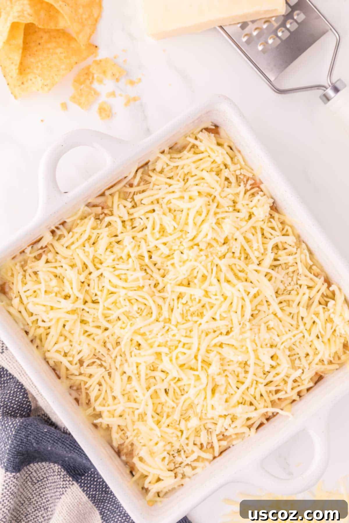 Rich Cream Cheese Bean Dip 6 A hand sprinkling shredded Monterey Jack cheese over the bean dip mixture in a baking dish