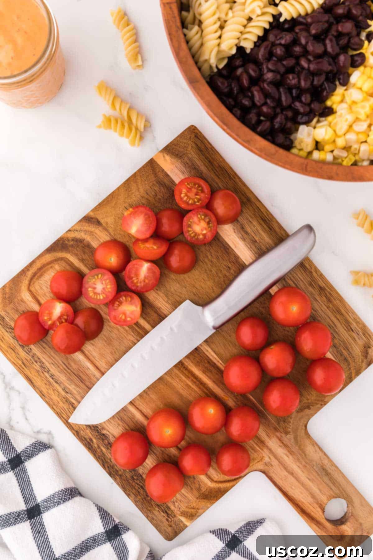 Zesty Southwest Pasta Delight 6 Bright red cherry tomatoes, halved and scattered on a wooden cutting board, prepped for the salad.