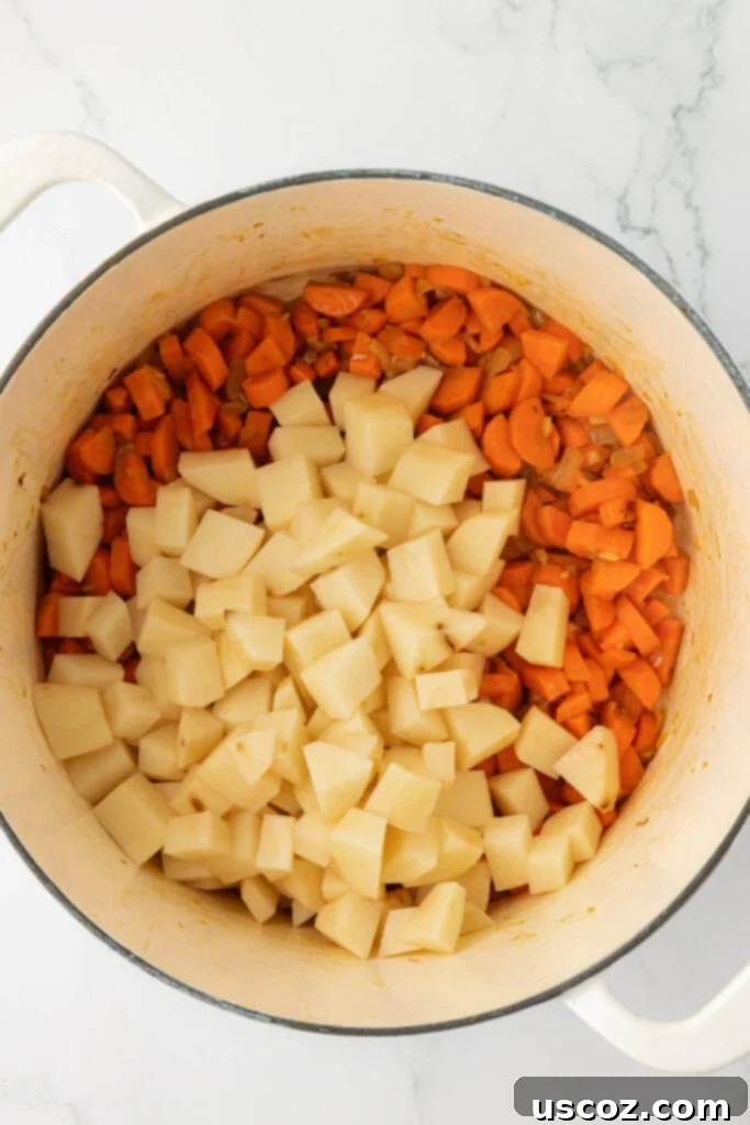 Velvet Veggie Delight 9 Diced potatoes being added to the pot with carrots, onions, and garlic, preparing for the liquid addition.