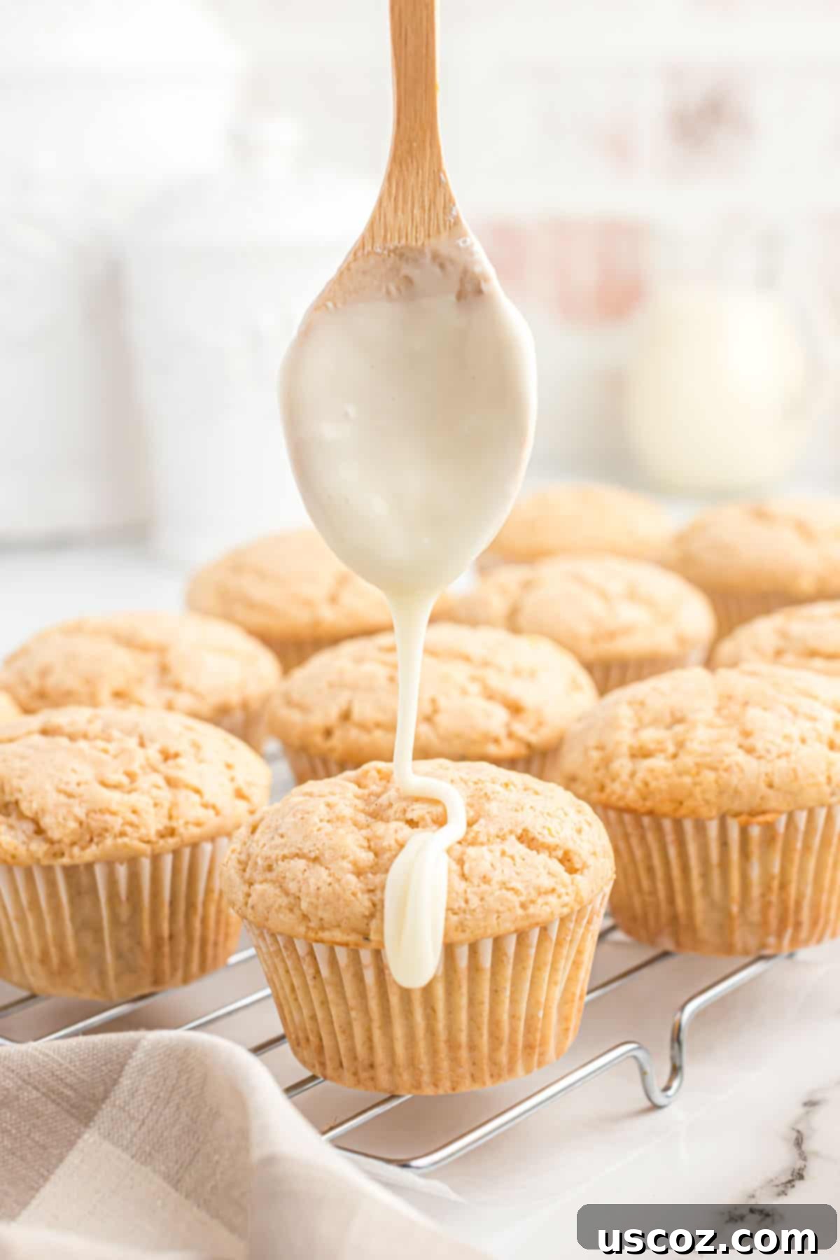 Holiday Eggnog Muffins 10 A freshly baked eggnog muffin being drizzled generously with homemade eggnog icing on a wire rack.