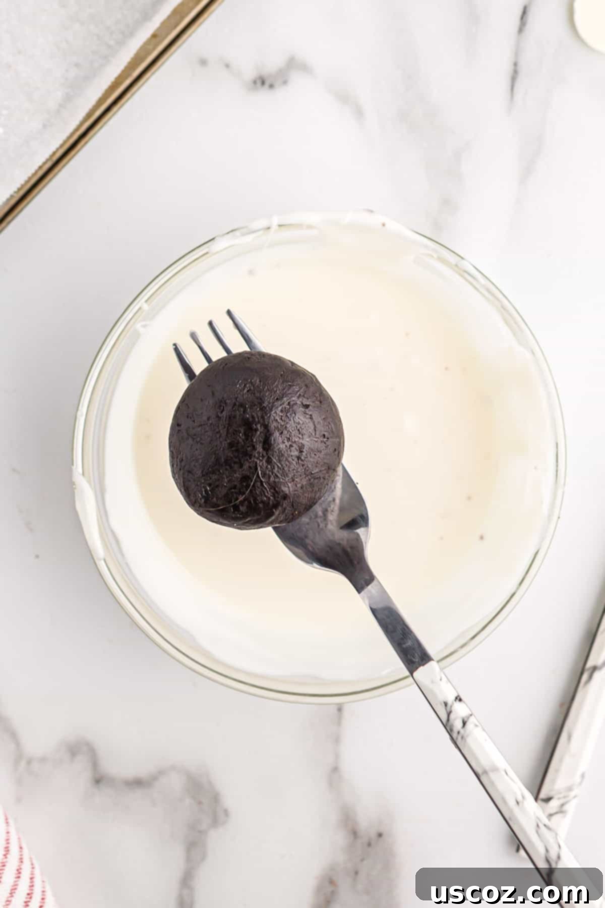 Oreo Truffles 8 A hand dipping an Oreo ball into a bowl of smooth, melted white vanilla chocolate, creating an elegant coating.