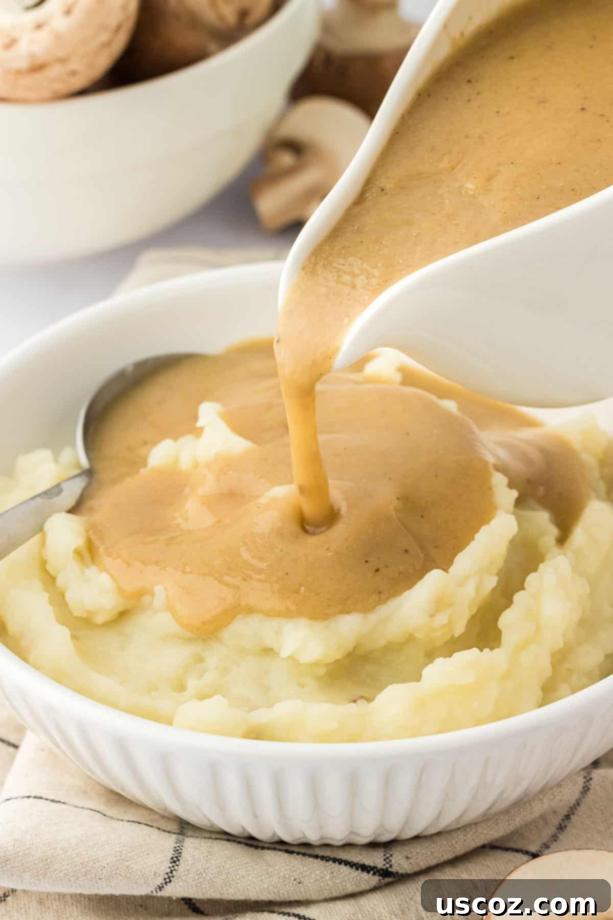 Perfect Vegetarian Gravy 22 Someone pouring hot vegetarian gravy from a white gravy boat over a plate of mashed potatoes.