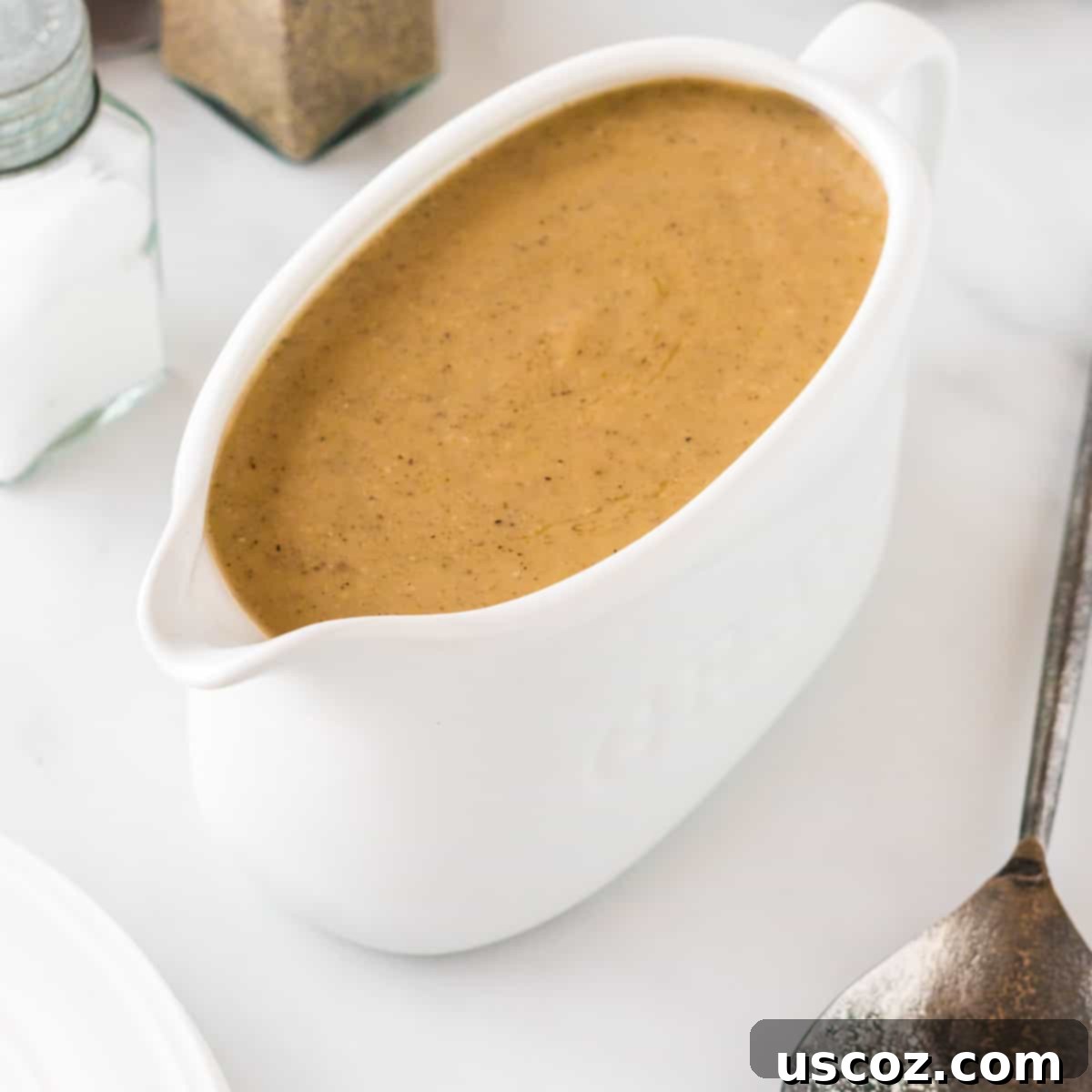 Perfect Vegetarian Gravy 26 A elegant white gravy boat filled with smooth, golden-brown vegetarian gravy on a festive table setting.