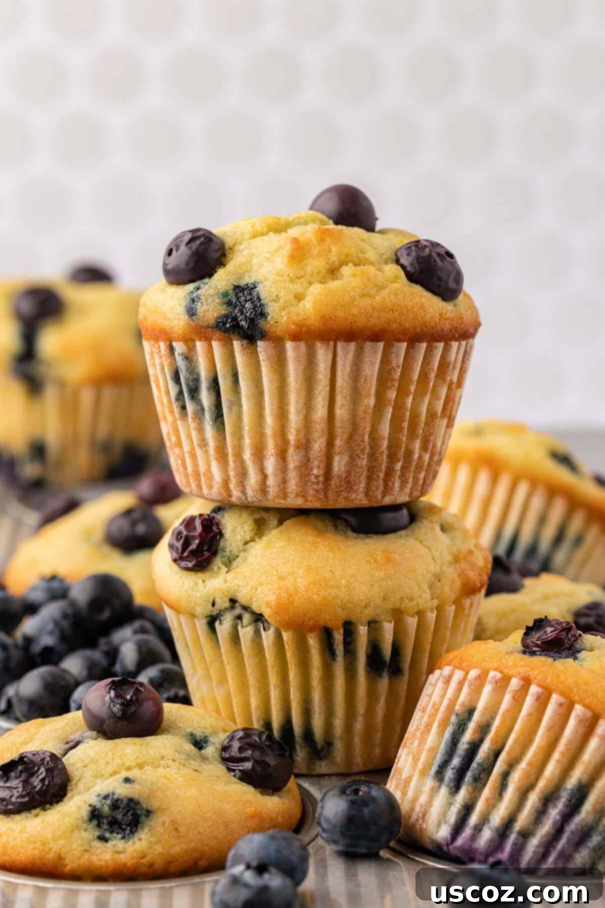 Sumptuous Sour Cream Blueberry Muffins 14 Stacked sour cream blueberry muffins on a white plate, showcasing their fluffy tops and blueberry distribution.