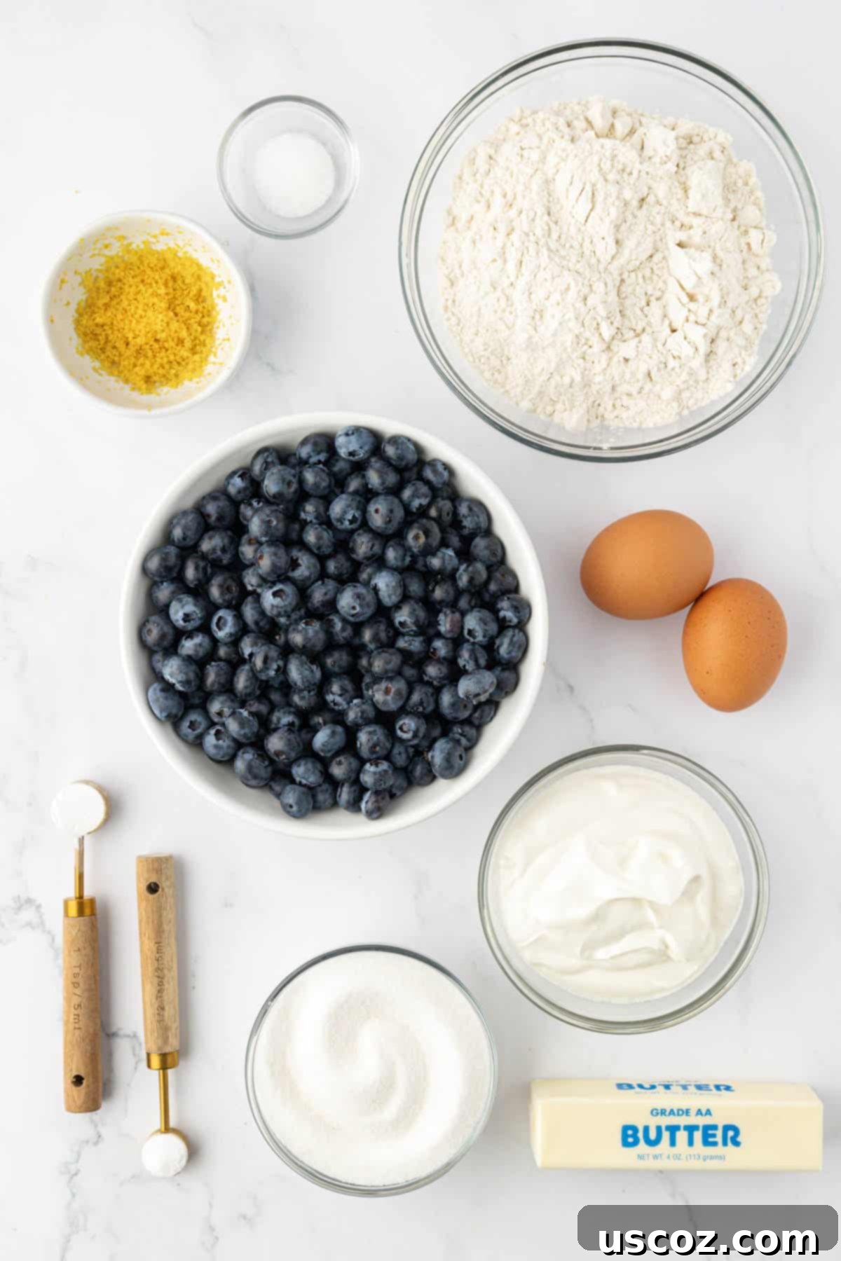 Sumptuous Sour Cream Blueberry Muffins 4 All ingredients laid out on a table to make sour cream blueberry muffins, including flour, sugar, eggs, butter, sour cream, lemon, and fresh blueberries.