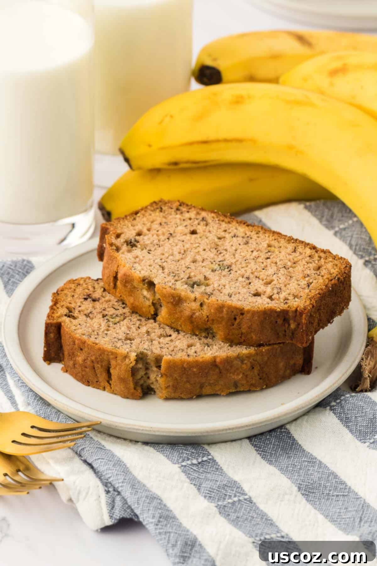 Ultimate Moist Banana Bread 16 Two generous slices of classic homemade banana bread, one with a dollop of butter, served on a white plate.