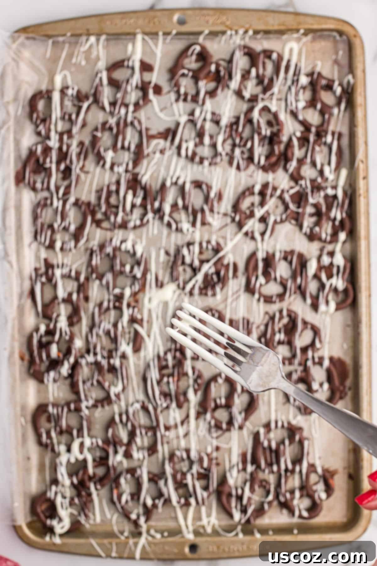 Chocolate Pretzel Perfection 9 A hand expertly drizzling melted white chocolate over a tray of dark chocolate covered pretzels, adding an artistic touch.