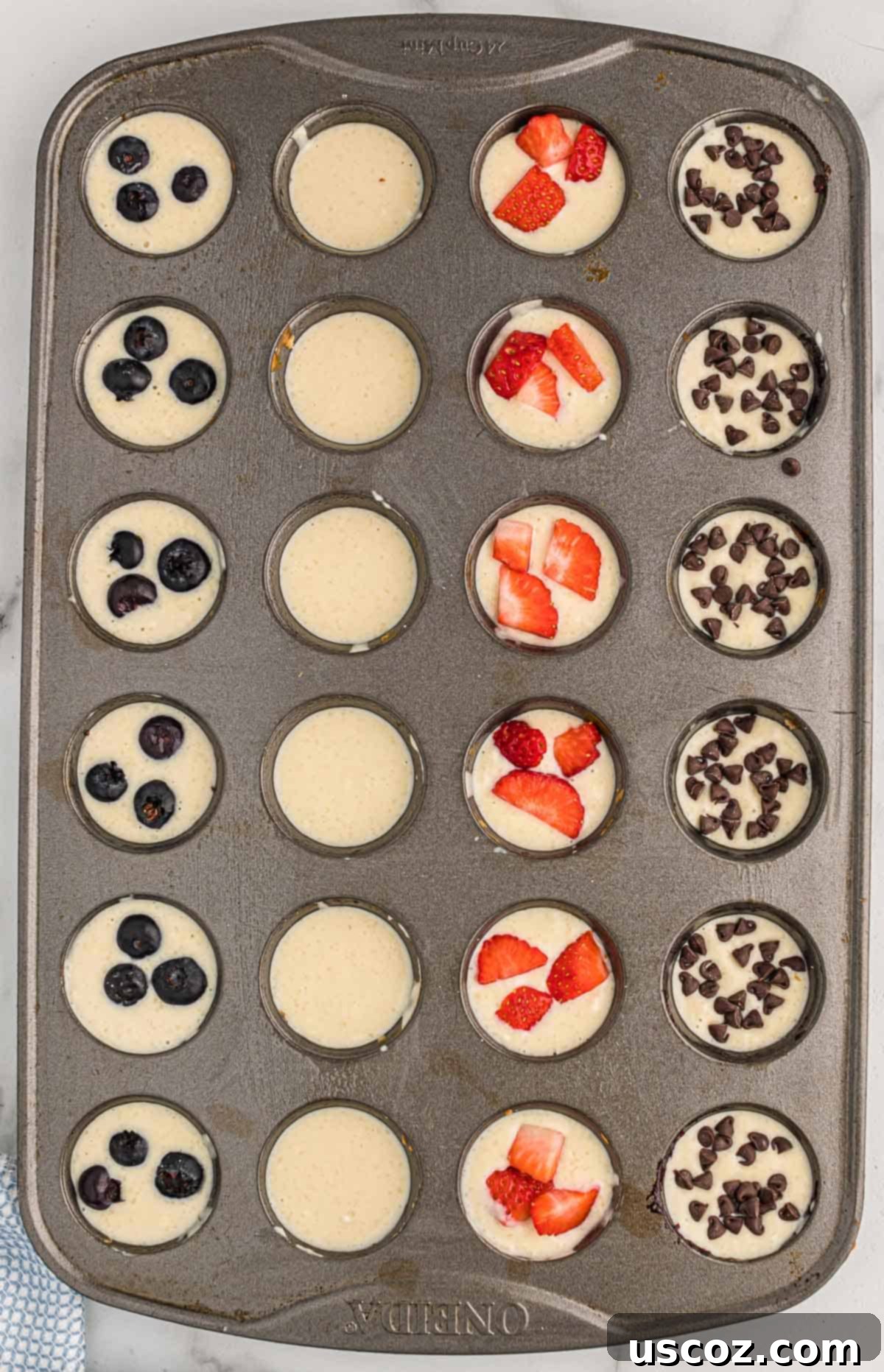 Breakfast Pancake Bites 9 A mini muffin tin filled with batter, topped with various mix-ins like blueberries, strawberries, and chocolate chips.