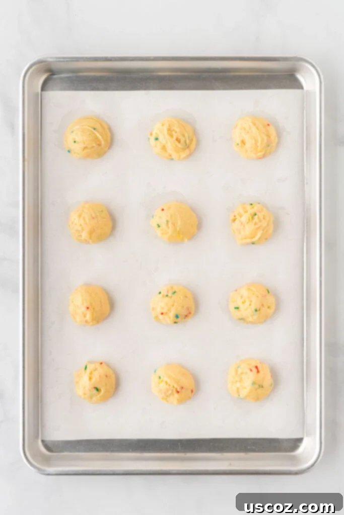 Simple Cake Mix Delights 6 Rows of scooped cake mix cookie dough balls neatly arranged on a parchment-lined baking sheet, prepared for baking.