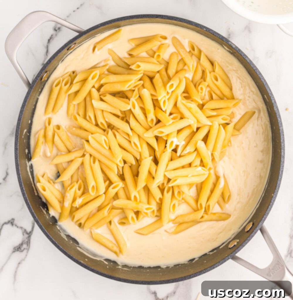 Decadent Creamy Penne 9 Adding perfectly cooked penne pasta into the rich cream sauce in a skillet