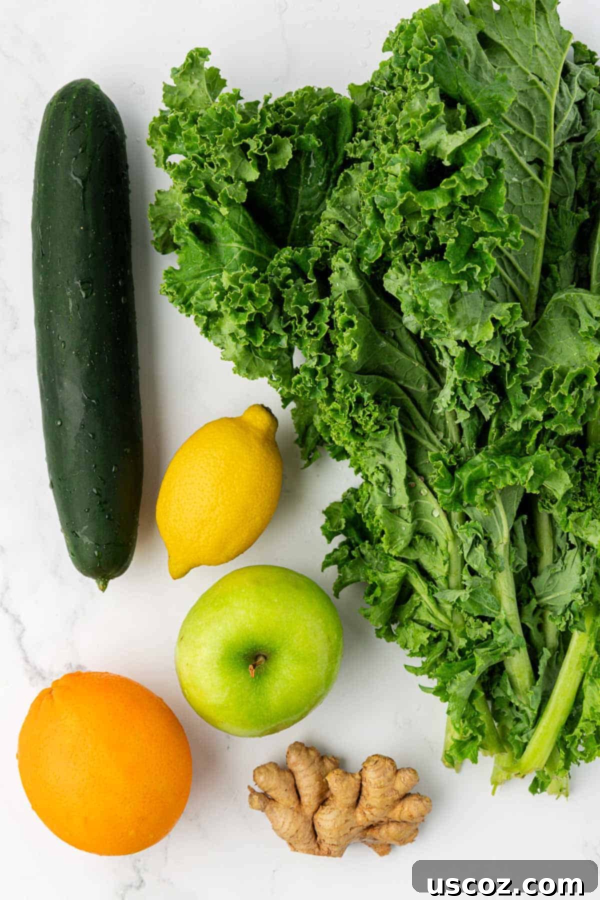 Emerald Elixir 4 A vibrant selection of fresh ingredients laid out for juicing: kale, cucumber, lemon, green apple, orange, and ginger.