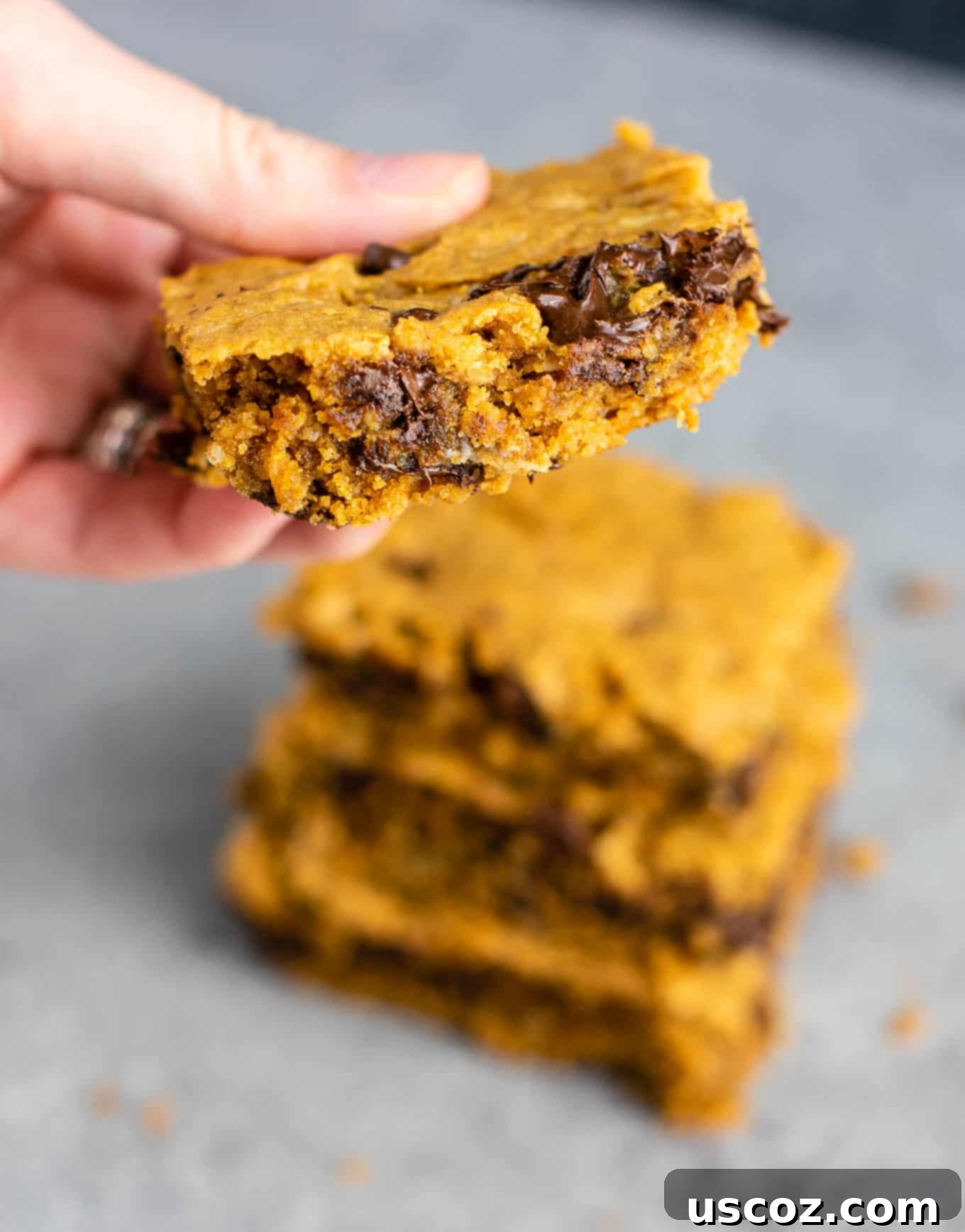 The Best Gluten-Free Cookie Bars 4 A hand reaching for a slice of moist and healthy gluten-free cookie bar, garnished with chocolate chips. This dairy-free dessert is a protein-packed and satisfying treat. #glutenfree #cookiebars #dessert #dairyfree #healthydessert #glutenfreedessert #glutenfreerecipe #glutenfreecookiebars