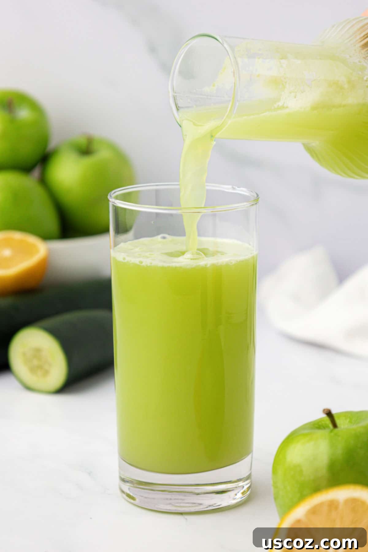 Emerald Zest Drink 7 Pouring freshly made green apple juice from a container into a glass.