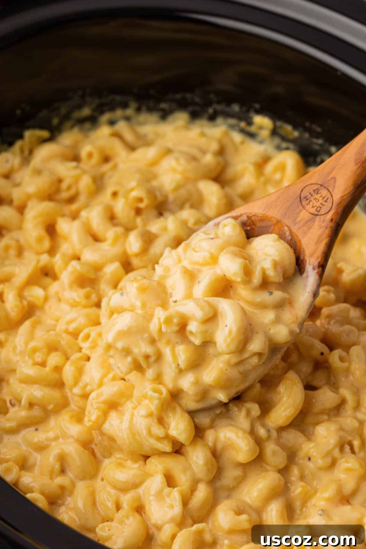 Creamy Slow Cooker Mac and Cheese 14 A wooden spoon taking a generous scoop of hot, bubbly mac and cheese from the crock pot