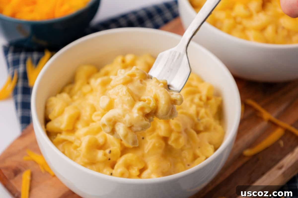 Creamy Slow Cooker Mac and Cheese 15 A fork taking a bite of creamy mac and cheese from a white bowl, showing melted cheese pull