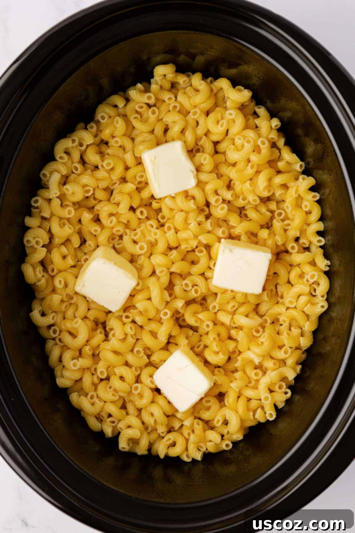 Creamy Slow Cooker Mac and Cheese 5 Cubed butter melting into par-cooked macaroni noodles in a slow cooker