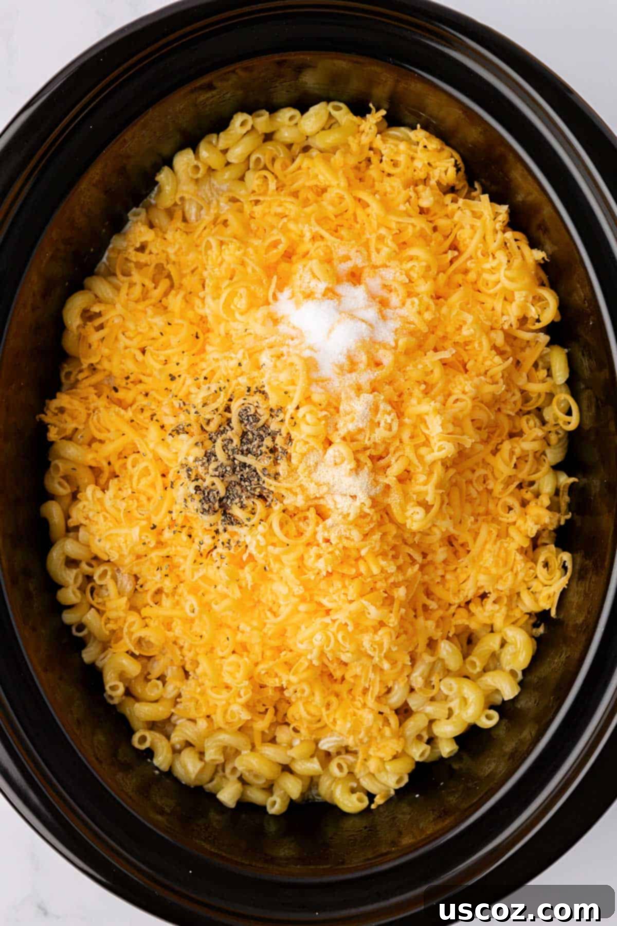 Creamy Slow Cooker Mac and Cheese 6 Adding freshly grated sharp cheddar cheese and a blend of spices to macaroni noodles in a slow cooker