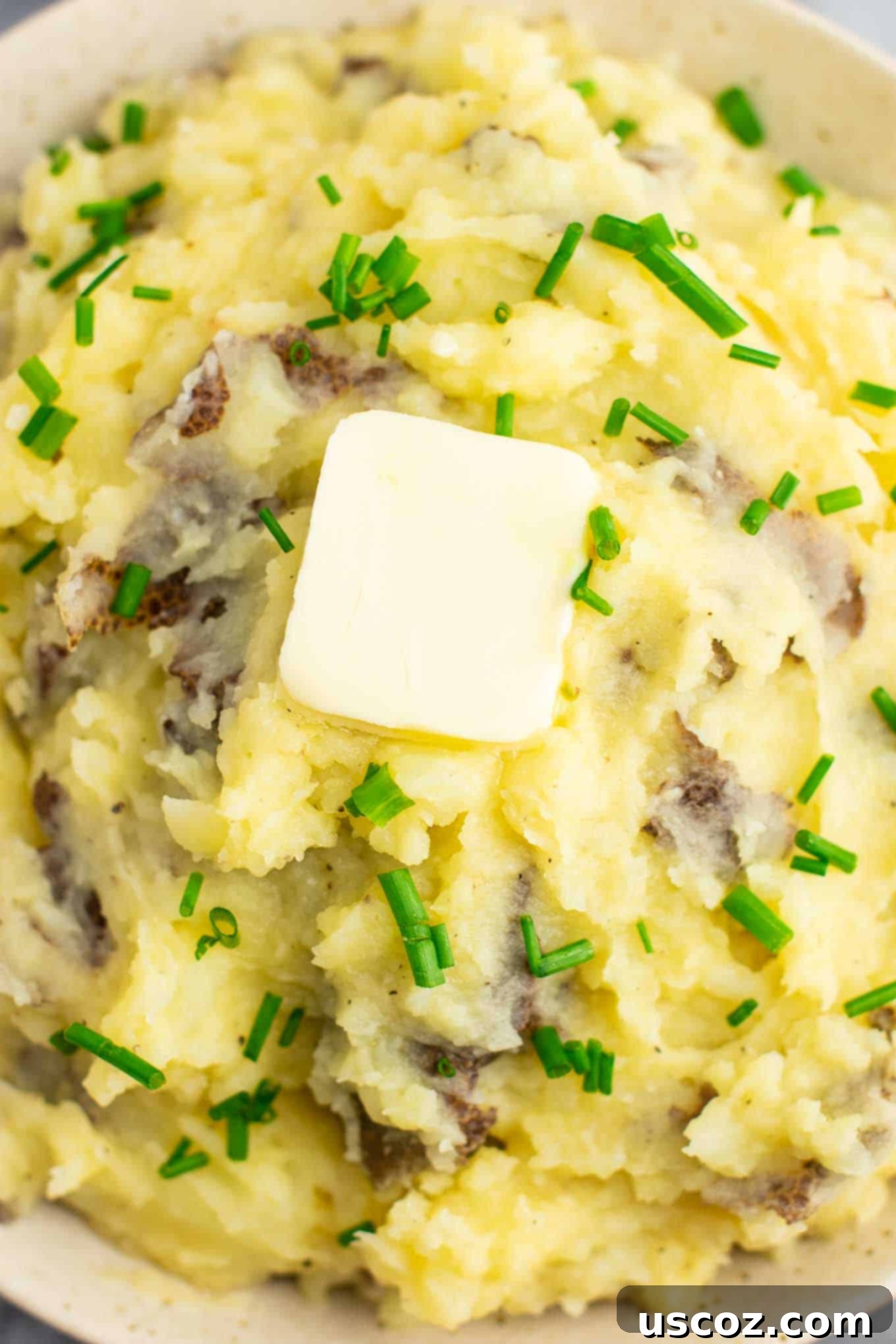 Creamy Vegan Mashed Potatoes 7 A large bowl of vegan mashed potatoes generously topped with melted vegan butter and a sprinkle of fresh chives, ready for serving.