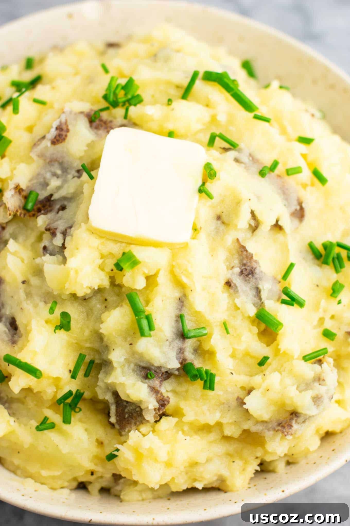 Creamy Vegan Mashed Potatoes 10 A large bowl of smooth vegan mashed potatoes, artfully garnished with melted vegan butter and fresh chives, presented on a rustic wooden surface.